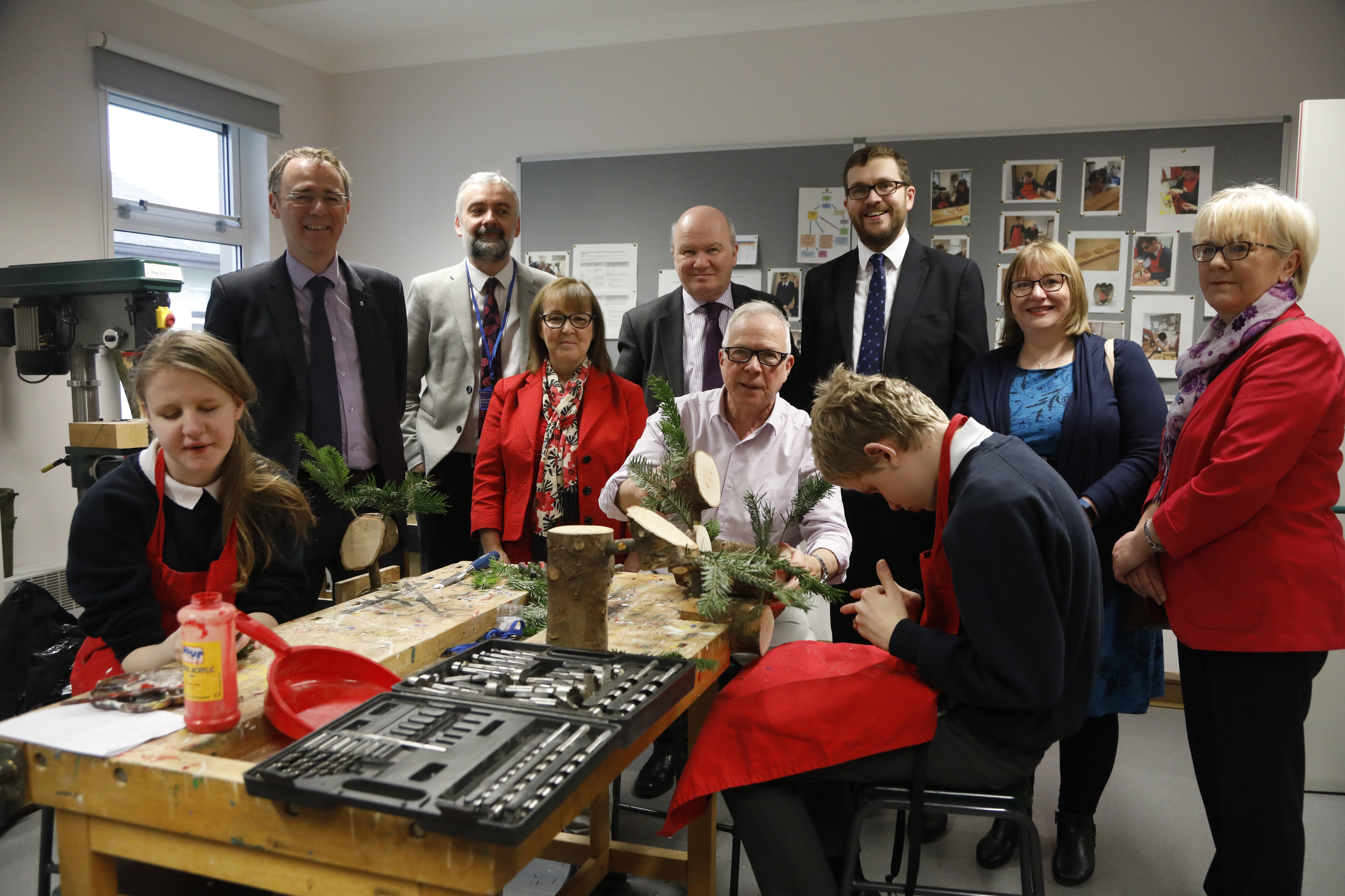 Picture shows Committee Members visiting a workshop at the Royal Blind School with two pupils and a teacher craft-making with pieces of wood and foliage.
